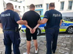 dwóch umundurowanych policjantów prowadzi zatrzymanego mężczyznę