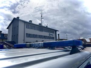 na pierwszym planie sygnalizator świetlny na dachu radiowozu policyjnego z napisem Policja, w tle budynek komendy Policji