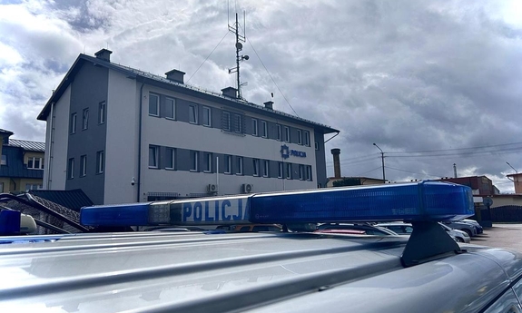 na pierwszym planie sygnalizator świetlny na dachu radiowozu policyjnego z napisem Policja, w tle budynek komendy Policji