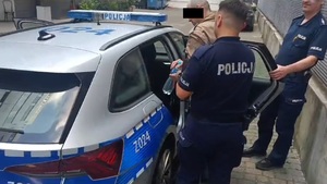 dwaj policjanci z zatrzymanym mężczyzną przy radiowozie policyjnym