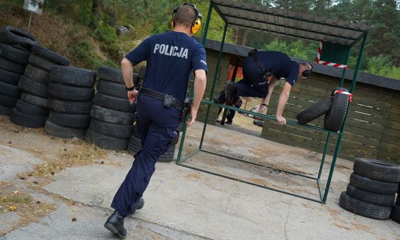 policjant biegnie, przed nim inny policjant przeskakuje przeszkodę