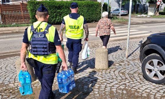 policjanci pomagają seniorce nieść wodę