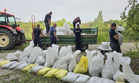 policjanci układają worki z piaskiem, które są rozładowywane z przyczepy