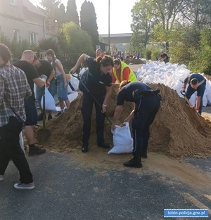 Policjantki wraz z innymi ludźmi sypią piasek do worków