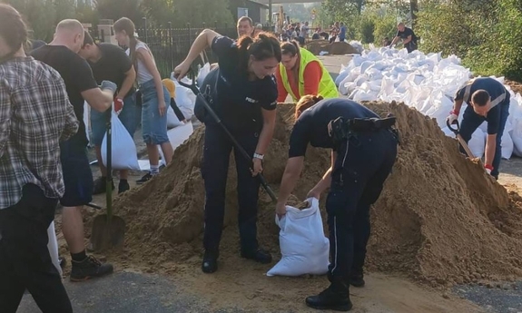 Policjantki wraz z innymi ludźmi sypią piasek do worków