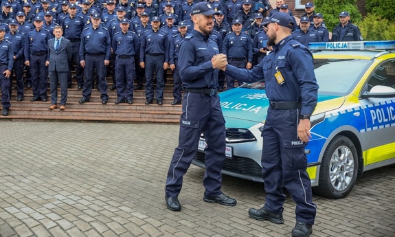 grupa policjantów stojąca na schodach i radiowóz