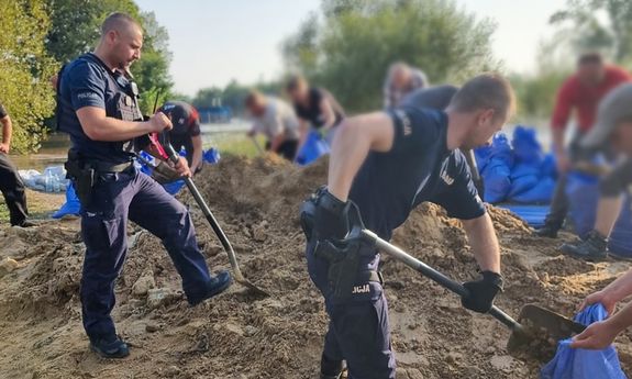 policjanci nakładają piach na łopaty i wrzucają go do worków