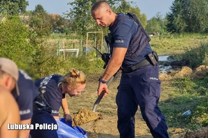 policjant wsypuje piach do worka trzymanego przez policjantkę