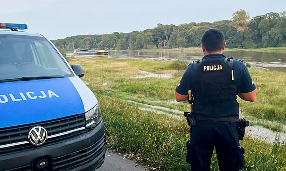 policjant stoi przy radiowozie i patrzy na wodę