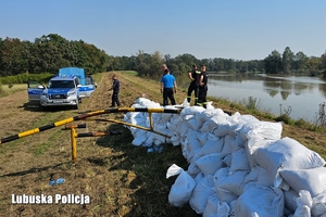 policjanci i strażacy na wale, na którym leżą worki z piaskiem