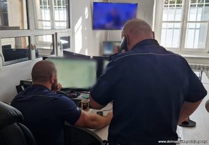 Policjanci na dyżurce odbierają telefon i monitorują dane na komputerze