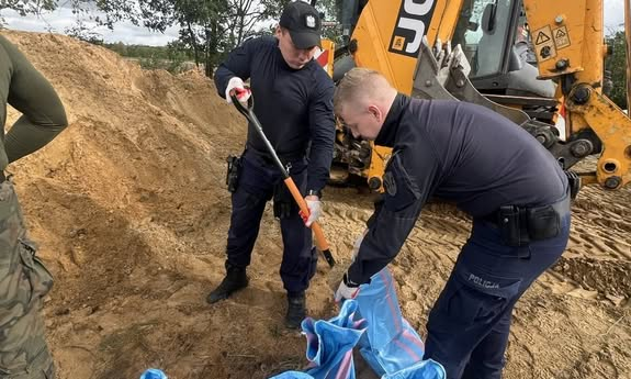 dwóch policjantów, jeden trzyma worek, a drugi wsypuje do worka piasek