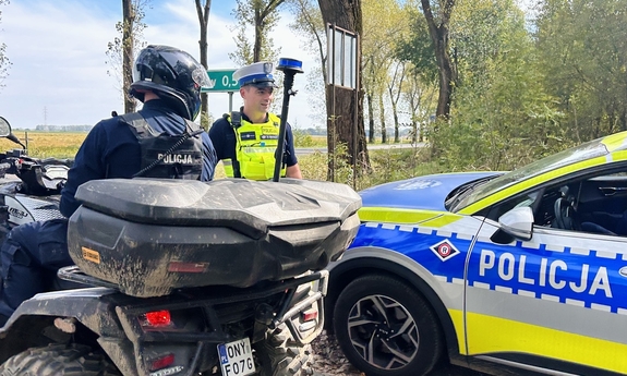 Dwaj policjanci ruchu drogowego. Jeden z nich siedzi na quadzie, a drugi stoi obok radiowozu.