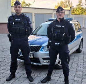 dwóch policjantów stoi przed radiowozem