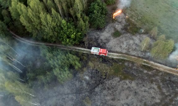 wóz strażacki widoczny z lotu ptaka, dym zakrywa część obrazka, lasy koloru zielonego widoczne z góry.