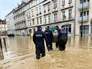 policjanci wspólnie niosą kobietę przez wodę