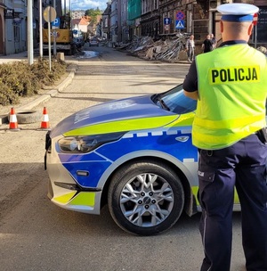 policjant stoi obok radiowozu, przed radiowozem jest zalana i zniszczona woda.