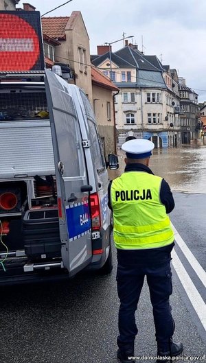 policjant stoi obok radiowozu, przed nim zalana droga.