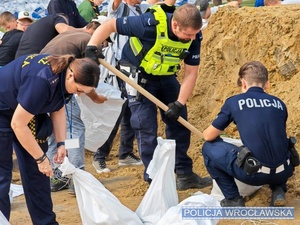 policjanci kopią piasek i wsypują go do worków