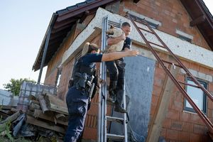 policjant schodzi po drabinie z psem na rękach, asekuruje go policjantka