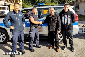 Policjanci i inni mężczyźni stoją przed radiowozem,