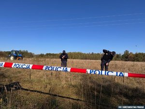 Funkcjonariusze na trawiastym terenie w trakcie poszukiwań. Na pierwszym planie taśma z napisem Policja odgradzająca teren.