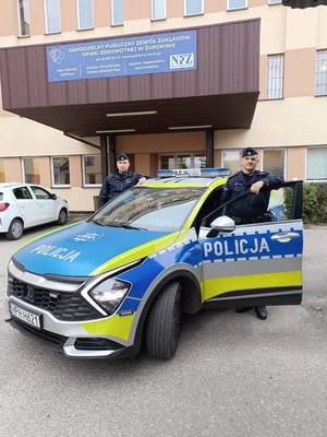 umundurowani policjanci stoją przy oznakowanym radiowozie.