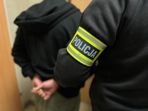 Funkcjonariusz z opaską policja prowadzi zatrzymanego.