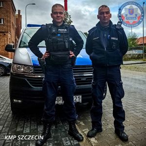 Dwaj umundurowani policjanci stoją przed policyjnym busem.