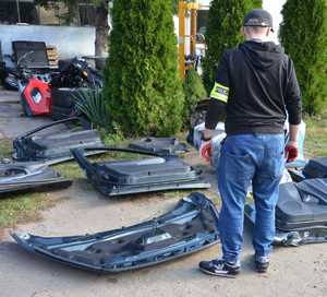 Na ziemi leży kilka części karoserii samochodowej. Obok stoi policjant.