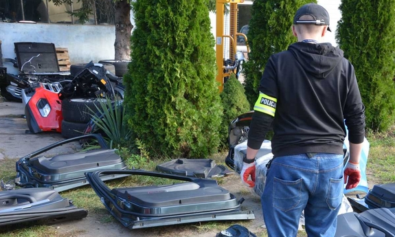 Na ziemi leży kilka części karoserii samochodowej. Obok stoi policjant.