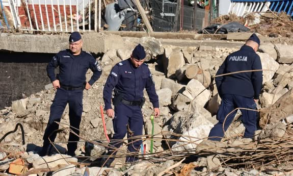 3 policjantów stoi na gruzach po swoim posterunku.