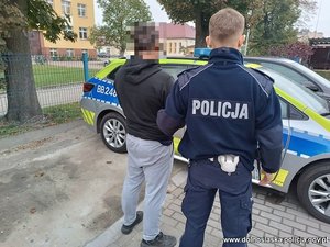 policjant w mundurze stoi obok zatrzymanego.