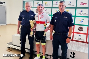 Policjant - kolarz w sportowym stroju stoi pomiędzy dwoma umundurowanymi oficerami Policji i trzyma w dłoni dwa puchary.