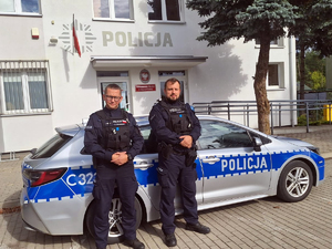 Dwaj policjanci stojący przy radiowozie policyjnym.