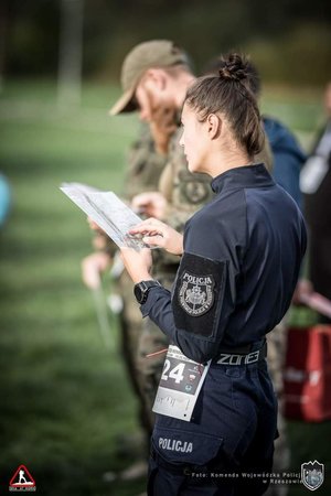 policjantka stoi bokiem i czyta mapę.