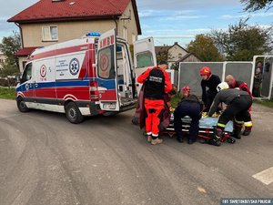 Na zdjęciu ratownicy pogotowia i strażacy pomogą w transporcie kobiety na noszach do karetki.