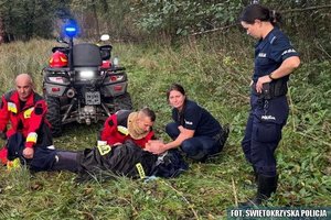 Na zdjęciu umundurowani policjanci i strażacy w trakcie odnalezienia kobiety. Odnaleziona leży na ziemi, policjantka trzyma jej głowie, a strażak się nad nią nachyla.