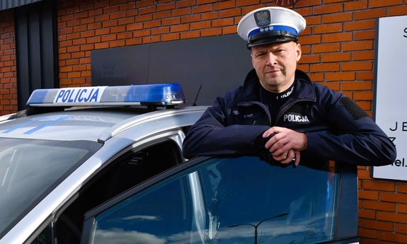 Policjant stoi przy radiowozie.