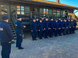 Oficer Policji stoi przed oddziałem ustawionym w dwuszeregu.