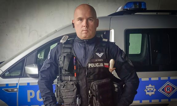 Umundurowany policjant stoi przy radiowozie.