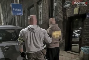 Na zdjęciu policjant z zatrzymanym mężczyzną na przeciwko samochodu. Obok budynek jednostki Policji.