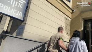 Na zdjęciu policjant prowadzi zatrzymaną kobietę do budynku komendy.