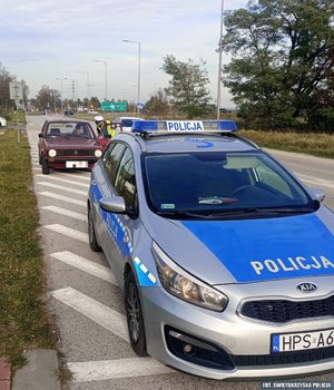 na pierwszym planie stoi radiowóz, w tle wiśniowy volkswagen.