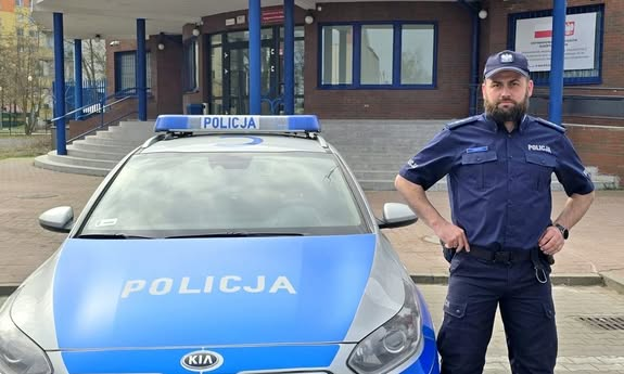 policjant stoi obok radiowozu.