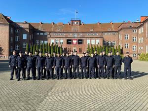 Funkcjonariusze Samodzielnego Pododdziału Prewencji Policji (SPPP) w Legnicy w mundurach stoją w dwuszeregu. W tle widoczny jest budynek.