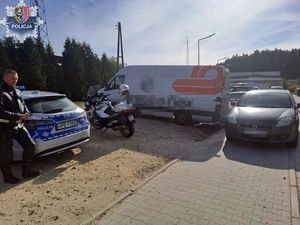 Policjant stoi koło radiowozu, z boku widoczny jest samochód dostawczy.