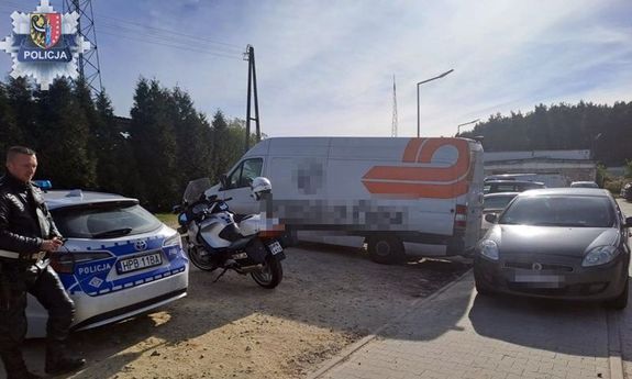 Policjant stoi koło radiowozu, z boku widoczny jest samochód dostawczy.