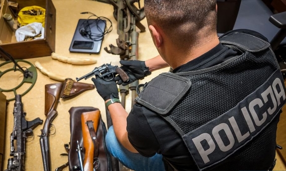 Zabezpieczona broń leży na podłodze, obok policjant.