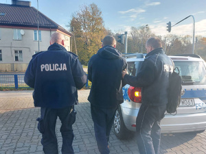 Dwaj policjanci prowadza zatrzymanego mężczyznę do radiowozu.